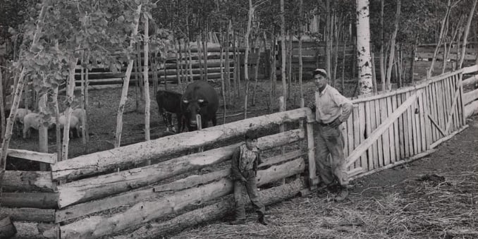Photograph of Antoine Bulldog of Beaver First Nation at the Boyer River Reserve, standing beside the pasture fence with his young son.